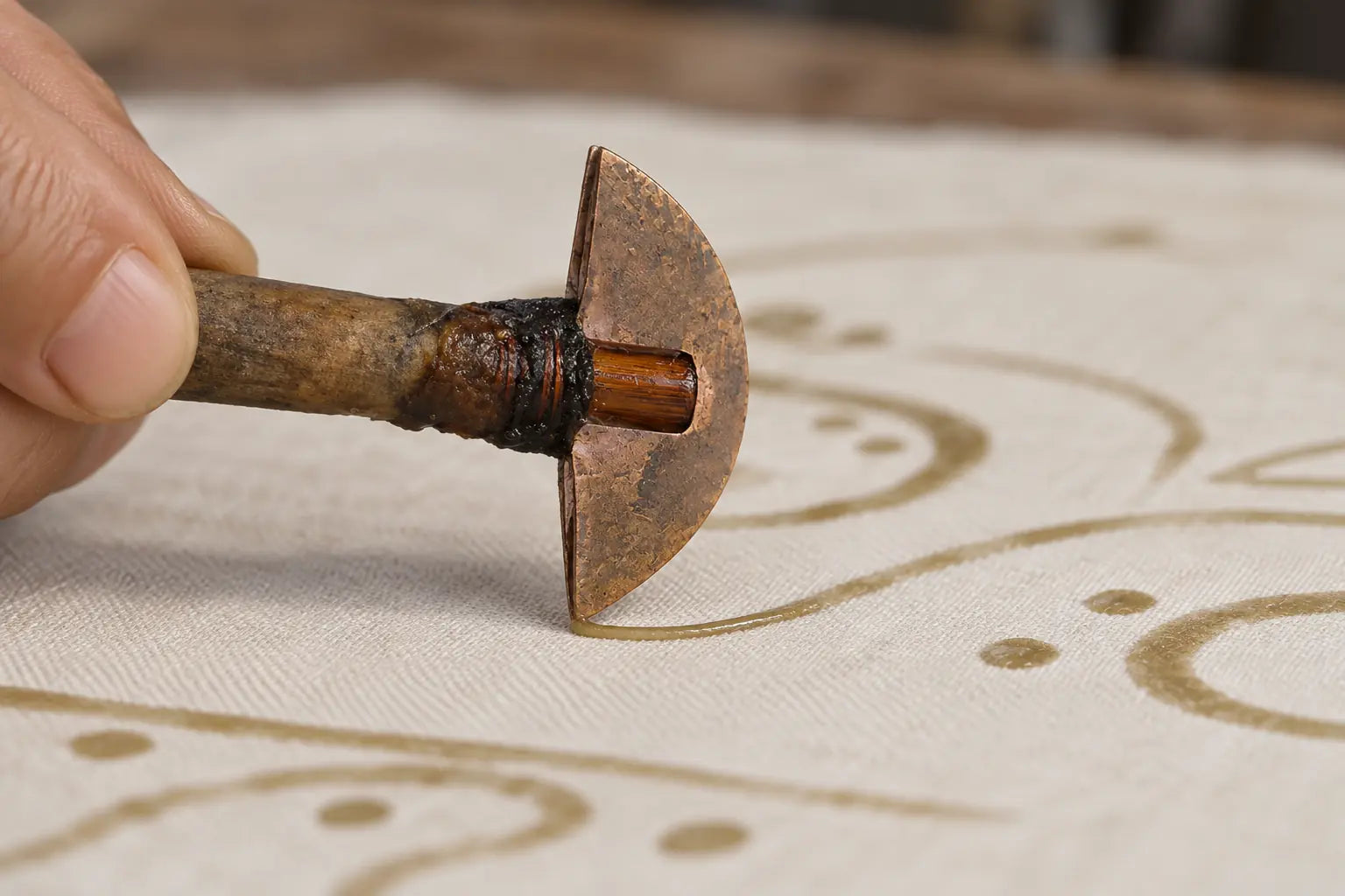 Craft illustration of a wax knife drawing a reserved line on cotton cloth