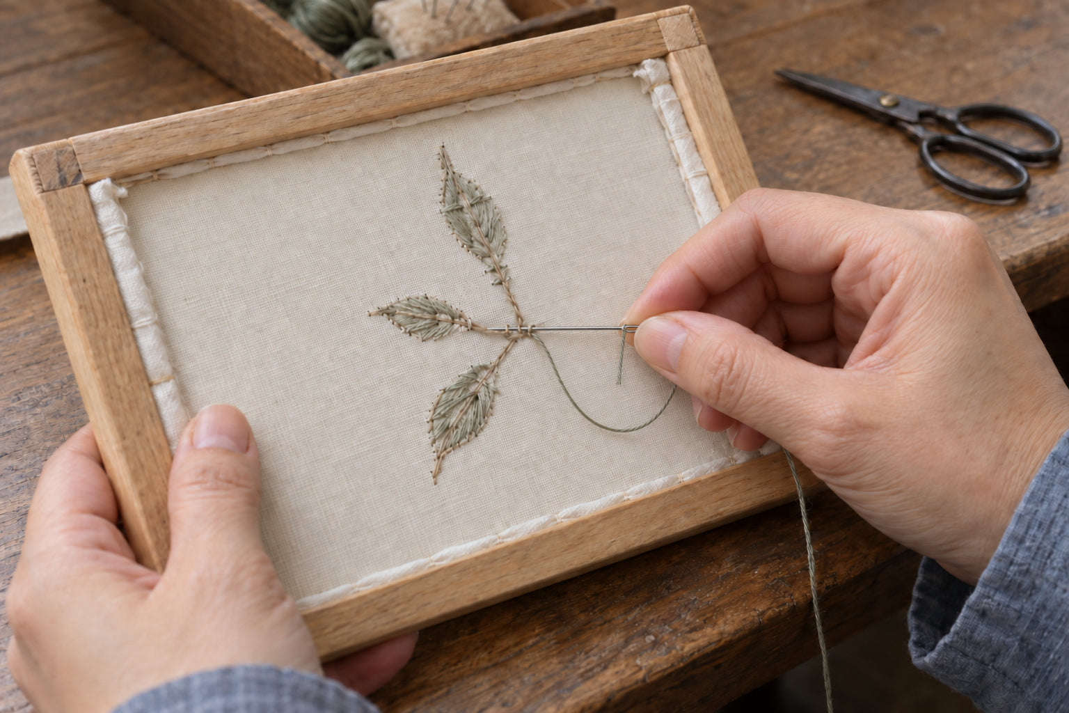 Craft illustration: a needle passing beneath existing stitches to secure a thread on the reverse of a leafy embroidery sample